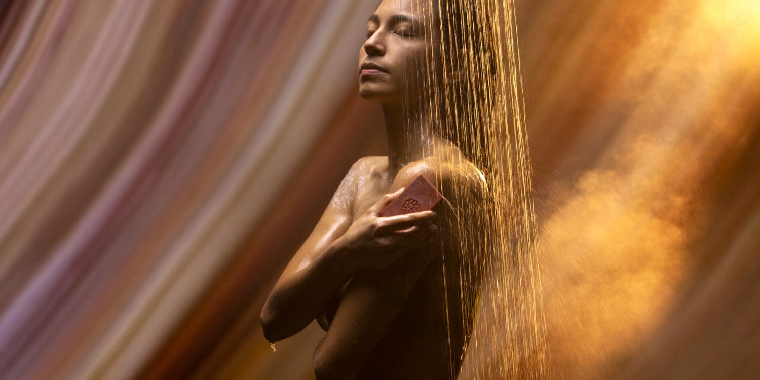 Woman using a JIVANTRA cleansing bar under a golden shower